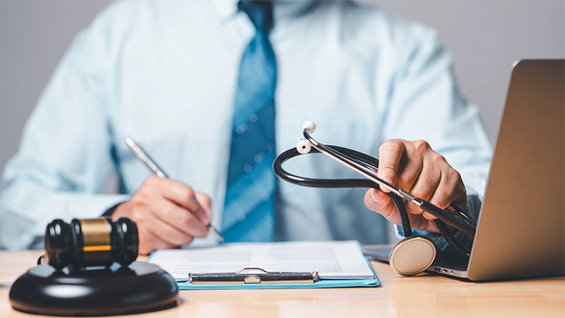 A personal injury lawyer holding a stethoscope, a gavel, and a laptop in a desk.