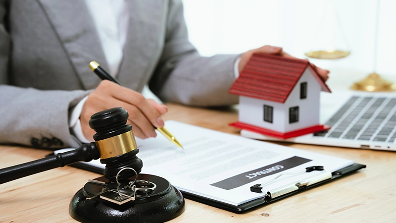 The attorney with a laptop near a house model, gavel, and contract.