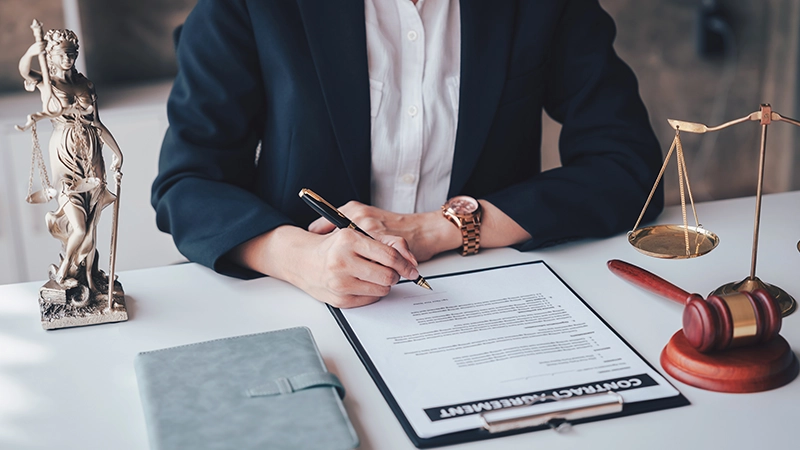 An adult Asian woman lawyer is signing a contract agreement document at her office.